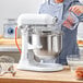 A woman pouring eggs from a glass bowl into a white KitchenAid countertop mixer.