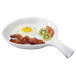 A white diamond skillet with a fried egg, bacon, and fruit on it.
