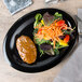 A GET textured black oval platter with meat and salad, including tomatoes and carrots.