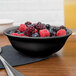 A black melamine bowl filled with berries on a table.