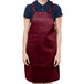 A woman wearing a burgundy Chef Revival bib apron with 1 pocket.