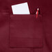 A burgundy Chef Revival bib apron with a pocket holding a pen and paper.