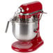 A red and silver KitchenAid commercial mixer on a white stand with a metal bowl.