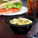 A black melamine bowl filled with pasta and a sandwich on a table.