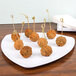 A close up of meatballs on toothpicks on a white triangular plate.