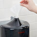 A hand putting a white cloth into a black plastic wall mount dispenser.