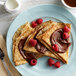 A plate of crepes topped with chocolate sauce and raspberries.