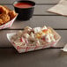A red check paper food tray with chicken and potato salad and fries on a table.