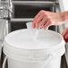 A hand putting WipesPlus Lemon Scent hand sanitizing wipes in a white bucket.