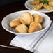 A round white melamine bowl filled with bread rolls on a table.