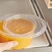 A hand holding a Choice translucent plastic deli lid over a container of brown liquid.