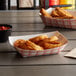 Two red check paper food trays filled with fried food and a black container of red sauce.