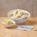 A white slanted melamine bowl filled with potato salad next to a bowl of coleslaw.