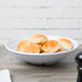 A white Milano melamine bowl filled with rolls on a table.