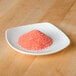 A small white plate with a pile of red salt on it.