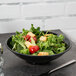 A black Milano melamine bowl filled with salad topped with croutons and tomatoes.