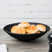 A Milano black melamine bowl filled with rolls on a table.