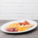 A white Milano melamine oval platter with cheese, crackers, and sausage on it.