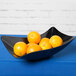 A black GET San Michele melamine bowl filled with oranges on a table.