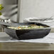 A black square melamine bowl with food in it.
