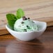 A white American Metalcraft sauce cup filled with mint chocolate chip ice cream and mint leaves.