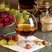 A Libbey brandy glass filled with brown liquid next to grapes and nuts.