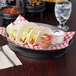 A table with a plate of tacos on a red and white checkered surface served in an oval charcoal deli server with a cup of salsa.