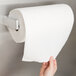 A hand using a Bobrick paper towel roll holder to dispense a paper towel.