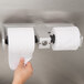 A hand pulling a roll of toilet paper from a Bobrick toilet paper dispenser.