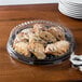 A clear plastic lid covering a round tray of cookies on a table.