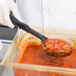 A person in white gloves using a Vollrath solid black spoodle to serve red sauce.