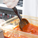 A gloved hand uses a Vollrath High Heat Solid Oval Nylon Spoodle to scoop red sauce from a glass container.
