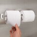A hand reaching for a roll of toilet paper in a metal toilet paper holder.