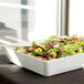An American Metalcraft rectangular white melamine bowl filled with salad with strawberries and lettuce.