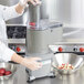 A woman in a white coat using a Waring continuous feed head cover on a food processor to slice potatoes.