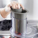A hand in a plastic glove using a Waring large gray pusher to juice in a food processor.