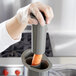 A person in a plastic glove using a Waring small grey pusher to put a carrot in a food processor.