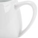 A close-up of a white ceramic creamer with a handle.
