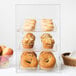 A Cal-Mil classic three tier acrylic bakery display case filled with pastries and bagels.