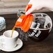 A person pouring coffee into a Grindmaster coffee decanter with an orange handle.