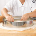 A person using an American Metalcraft stainless steel dough cutter to cut dough.