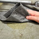 A hand using a Spilfyter gray absorbent pad to clean a spill on concrete.