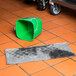 A green bucket on a tile floor with a Spilfyter Universal Gray absorbent pad inside.