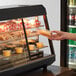 A hand placing a plastic container of food into an Avantco countertop heated display case.