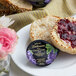 A close-up of a package of Dickinson's Pure Concord Grape Jam next to a plate of muffins with jam and flowers.