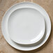A Homer Laughlin Ameriwhite Alexa bright white square china plate on a table with two empty plates on top.
