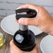 A hand using a black and silver Waring foil cutter to open a bottle of wine.
