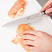 A person using a Mercer Culinary Japanese Gyuto knife to cut raw chicken on a cutting board.