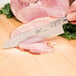 A Mercer Culinary MX3 Santoku knife cutting meat on a cutting board.