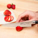 A person using a Mercer Culinary MX3 Japanese petty knife to cut strawberries on a plate.